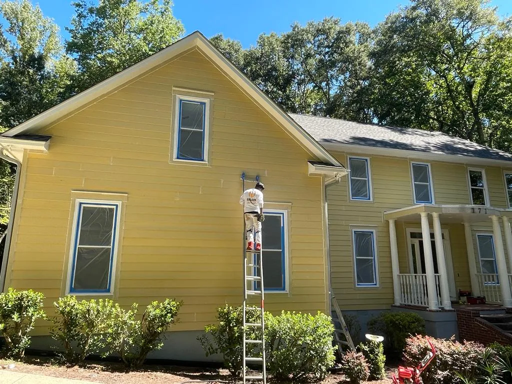 RIBAM crew painting a home's upper siding from a ladder